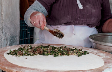 woman cooking gozleme traditional turkish pancakes with mince meat and green mediterranean herbs in wood oven