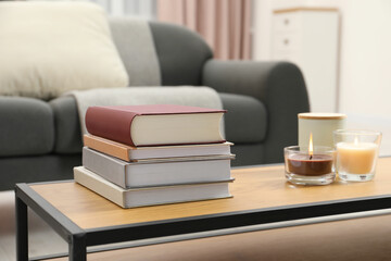 Books and burning candles on wooden table in living room
