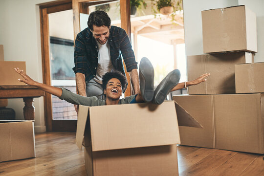 Happy couple, box and real estate moving in house or property in renovation or investment together. Interracial man and woman playing in living room with boxes for relocation, celebration or new home