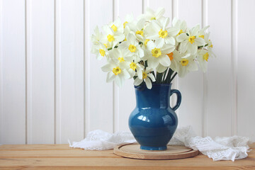 A bouquet of white daffodils on a wooden table and a place to copy. spring flowers in a blue jug.
