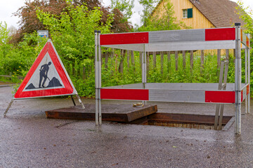 Mobile road sign with barrier at open manhole of district heating for maintenance work at City of Zürich district Schwamendingen on a rainy spring day. Photo taken May 11th, 2023, Zurich, Switzerland.