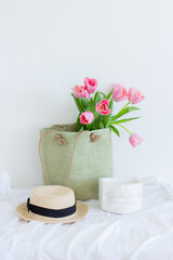 Pink tulips bouquet in green shopping bag, gypsum lips and a straw hat on white background copy space