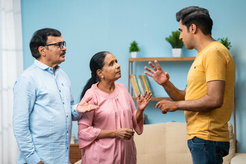 angry Indian adult son arguing with elderly senior parents at home - concept of irresponsibility,...