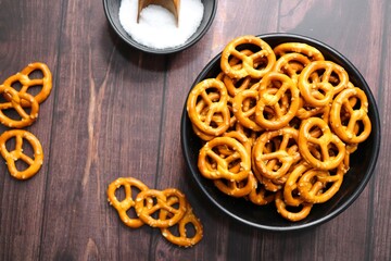 Crunchy pretzels in a black bowl are placed on a wooden table. A perfect salty party snack. copy space. crispy baked salt cookies or biscuits 