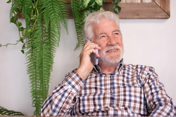 Portrait of bearded senior smiling man talking on mobile phone sitting at restaurant table