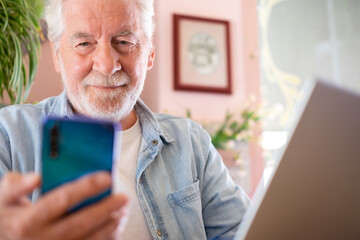 Smart work concept. Smiling senior man in coffee shop while working on laptop using mobile phone. Elderly man people enjoying free lifestyle doing job from remote
