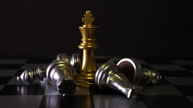 Cinematic shot of king chess pieces on a chess board, yellow figure is standing straight and other white figures are lying on side. 