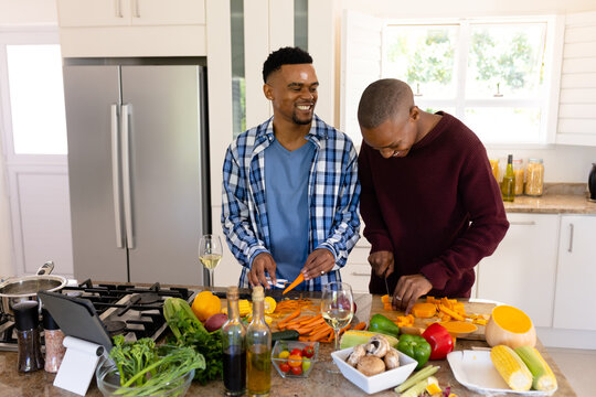 African american young gay couple smiling and chopping fresh vegetables on island in kitchen