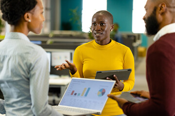 African american male and female coworkers discussing sales reports over laptop and digital tablet