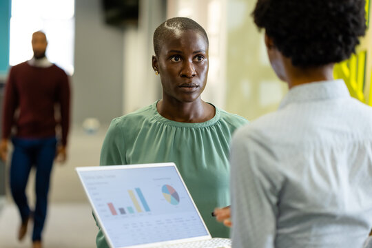 Rear view of african american businesswoman discussing charts over laptop with female coworker