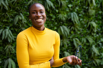 Portrait of african american young businesswoman with short hair holding eyeglass against plants