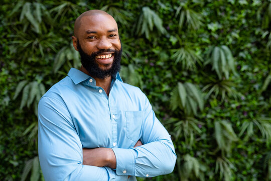 Portrait of cheerful bearded african american businessman with arms crossed standing against plants