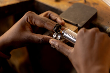 Close up of hands of african american worker making jewellery using tools at jewellery workshop