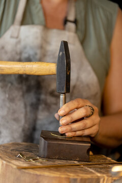 Midsection of caucasian female worker making jewellery using hammer at jewellery workshop