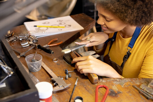 Happy biracial female worker making jewellery using tools at jewellery workshop