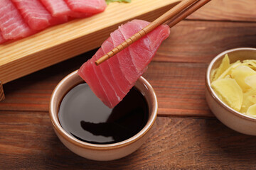 Dipping tasty sashimi (piece of fresh raw tuna) into soy sauce at wooden table