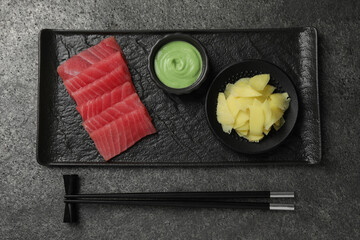 Tasty sashimi (pieces of fresh raw tuna) served with wasabi sauce and ginger slices on gray table,...