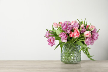 Beautiful bouquet of colorful tulip flowers on wooden table near light wall, space for text
