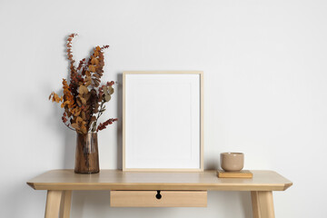 Empty photo frame, cup and vase with dry decorative leaves on wooden table. Mockup for design