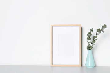 Empty photo frame and vase with decorative eucalyptus leaves on white table. Mockup for design