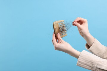 Woman untangling her lost hair from comb on light blue background, closeup and space for text....