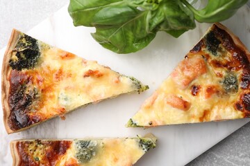 Pieces of delicious homemade salmon quiche with broccoli and basil on white board, top view