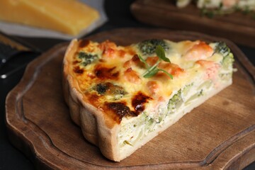 Piece of delicious homemade quiche with salmon and broccoli on wooden board, closeup
