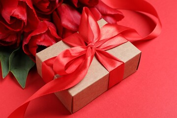 Beautiful gift box with bow and tulip flowers on red background, closeup