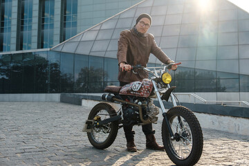 Shot of hipster man driving retro motorcycle looking at camera outdoors.