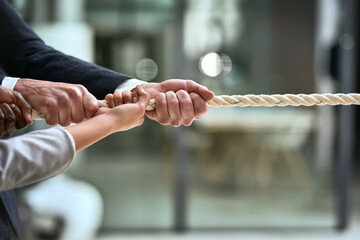 Hands, teamwork and rope with business people pulling during a game of tug of war in the office....