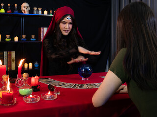 Asian sorceress woman cast a spell on magic blue crystal ball for oracle tell her about client fate before pick a tarot card on the red table