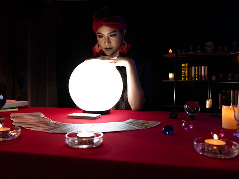 Asian fortune teller woman use crystal lamp light ball and tarot cards for reading customer life and paranormal belief in the dark room