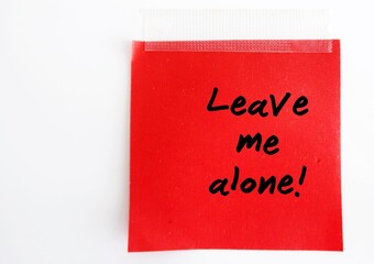 A red note with text written LEAVE ME ALONE ,on white background. Concept of  refrain from disturbing, interfering with someone, need private time.