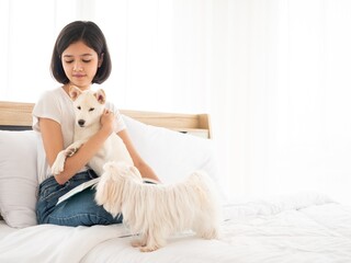 Asian pretty teen girl playing and hug Japanese Shiba Inu short hair and Maltese dog pet while reading a book productive activity in the morning at bedroom home
