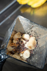 A view looking into a blender pitcher, featuring frozen banana, cacao nibs and peanut butter.