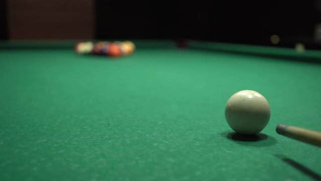 Close-up of a cue stick striking a triangle of billiard balls on a green table. Billiard sport