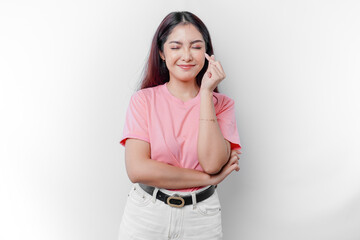 A happy young Asian woman wearing a pink t-shirt feels romantic shapes heart gesture expressing...
