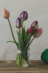 A bouquet of colored tulips and a sweater on a wooden table.