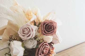 A view of a rustic rose floral bouquet against a white wall.