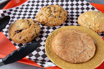 A view of several cookies on a tray, featuring chocolate chip, oatmeal raisin, snickerdoodle and macadamia nut.