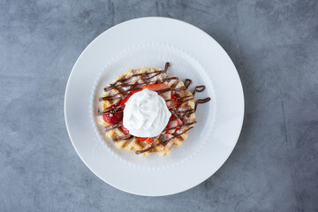A top down view of a waffle with sliced strawberries, whipped cream and hazelnut spread icing.