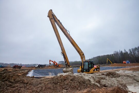 Ust-Luga, Leningrad oblast, Russia - November 16, 2021: Construction of chemical waste ditch. Caterpillar excavator with long boom dig pit