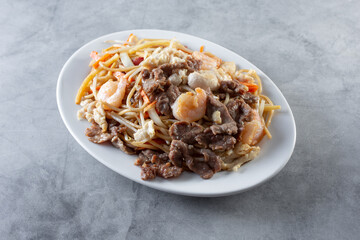 A view of a plate of chow mein, featuring beef, chicken and shrimp.
