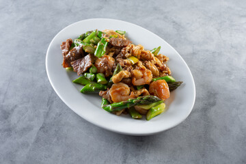 A view of an asparagus stir fry, featuring beef, chicken and shrimp.