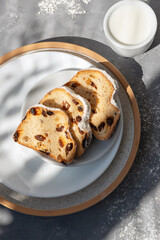 Sliced sweet fruit cake, traditional Christmas stollen on plate, milk cup on gray background with aesthetic sunlight shadows, lifestyle sweet morning breakfast concept