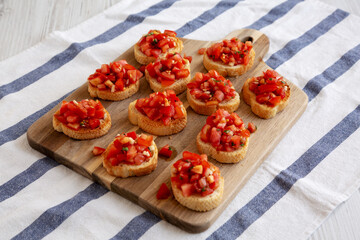 Homemade Italian Bruschetta Appetizer with Fresh Basil and Juicy Tomatoes on a Wooden Board, side view.