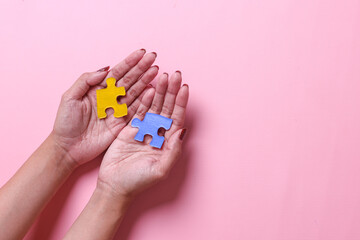 Colorful puzzle pieces on palms on pink color background. World autism  awareness day. 