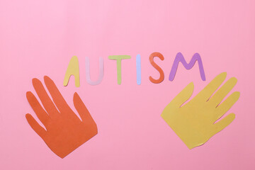 Colorful autism lettering with colorful paper hands shape isolated on pink background. Concept of autistic disorder.