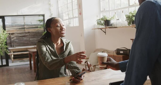 African american male barista giving takeaway coffee to female customer at coffee shop, slow motion