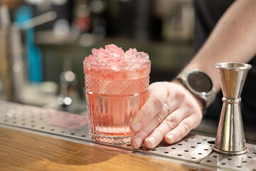 Bartender holding fresh delicious red summer cocktail in glass